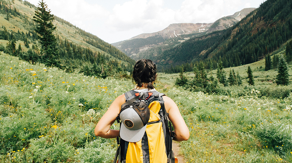 Back of woman with backpack walking through a hilly, green landscape